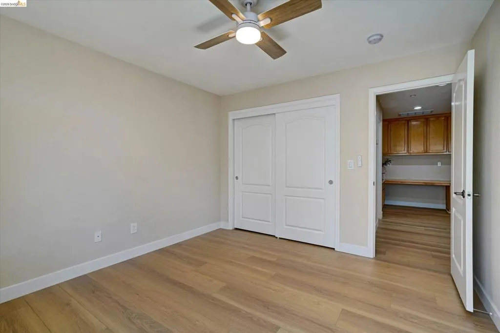 Room featuring wood-finish flooring, a ceiling fan with integrated lighting, and a closet with white sliding panel doors