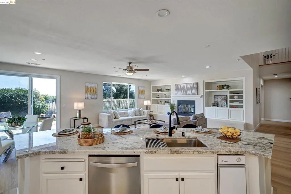 Spacious kitchen island with a granite countertop, undermount stainless steel sink, and integrated dishwasher, open to family room