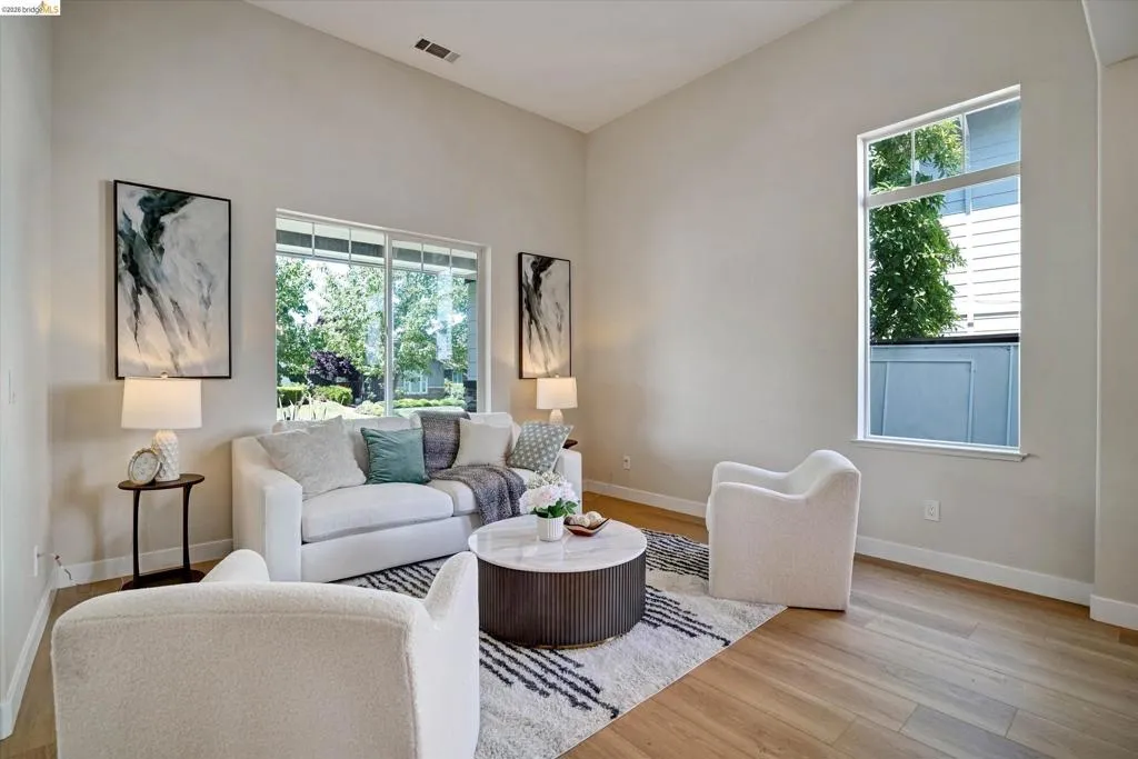 Vaulted ceiling living area featuring large windows, wood-finish flooring, and light-toned wall paint
