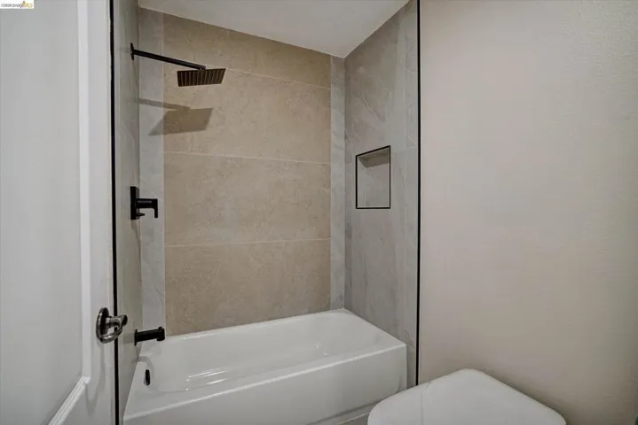 Bathtub shower combination featuring large format tile surround, a built-in shower niche, and matte black fixtures including a rain showerhead