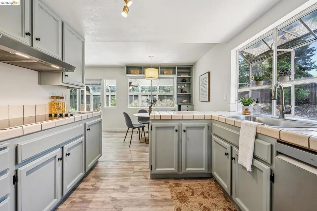Kitchen featuring light gray cabinetry, tile countertops, a stainless steel sink with a gooseneck faucet, and wood-finish flooring