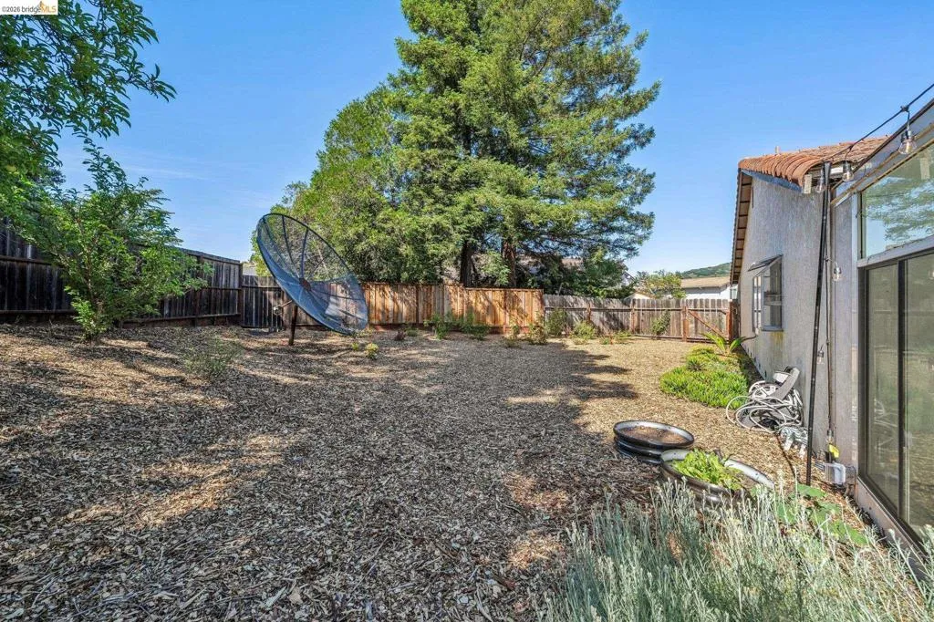Expansive rear yard featuring wood chip ground cover, perimeter wood fencing, and established trees