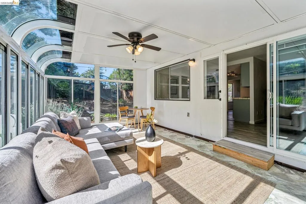 Sunroom featuring a curved glass roof, extensive glass paneling, durable stone flooring, a ceiling fan with integrated lighting, and direct access to interior spaces via sliding glass doors