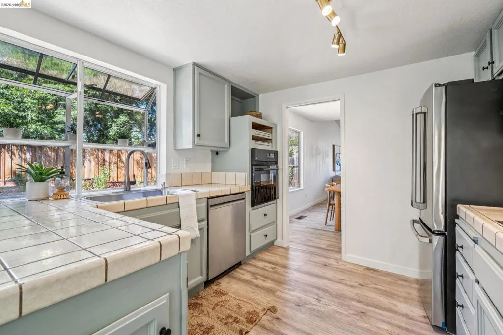 Kitchen featuring a stainless steel sink, tile countertops, light-toned cabinetry, stainless steel appliances, and wood-finish flooring
