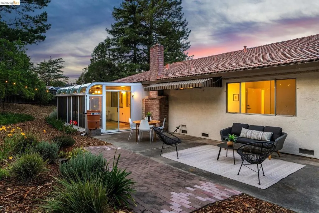 Expansive rear patio featuring a brick paver pathway, a sunroom extension with sliding glass doors, and a red tile roofline