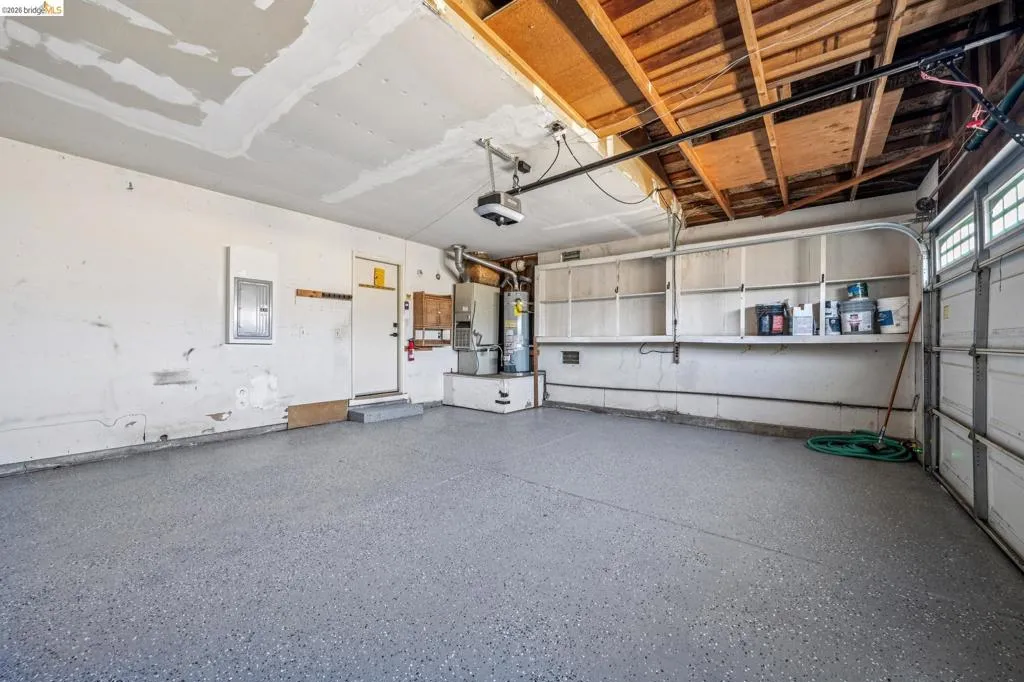 Garage featuring an epoxy-coated concrete floor, exposed wood ceiling beams, built-in shelving, an automatic garage door opener, and a water heater installation