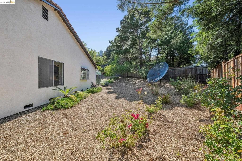 Rear yard featuring a wood chip ground cover, mature landscaping, and a wood fence perimeter