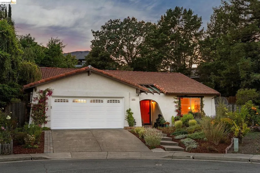 Stucco exterior residence featuring a terracotta tile roof, white garage door with window inserts, and an arched red entry door