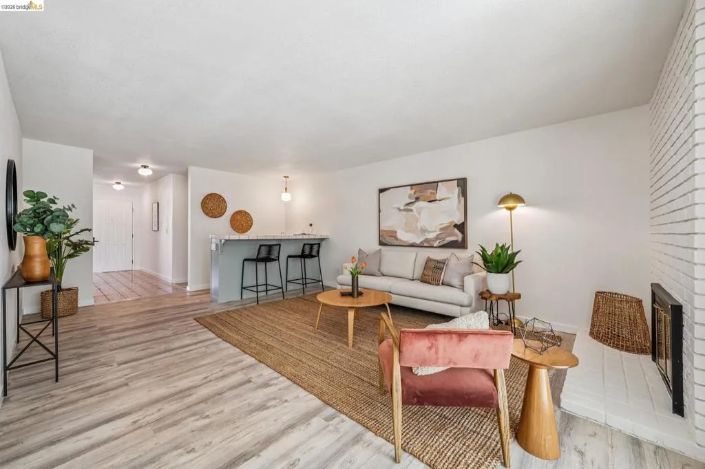 Open-concept living area featuring wood-finish flooring, a painted brick fireplace, a built-in breakfast bar, and recessed lighting