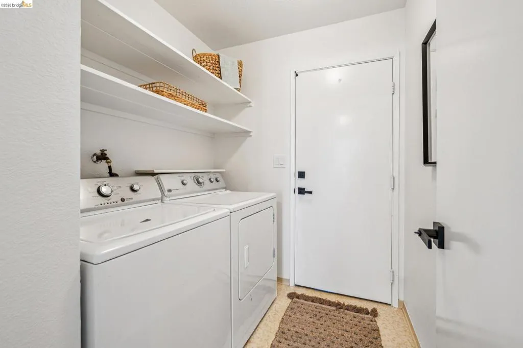 Dedicated laundry area featuring a white washer and dryer pair, brass utility faucet, and two integrated storage shelves