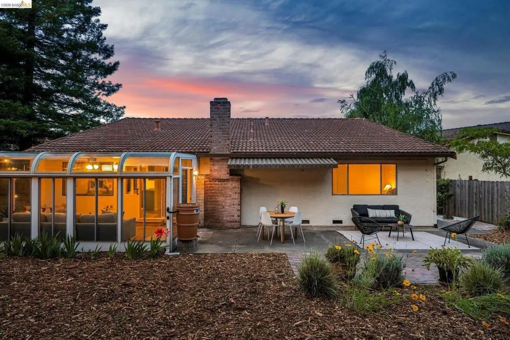 Rear exterior featuring a sunroom addition with curved glass panels, a tiled roof, and a red brick chimney