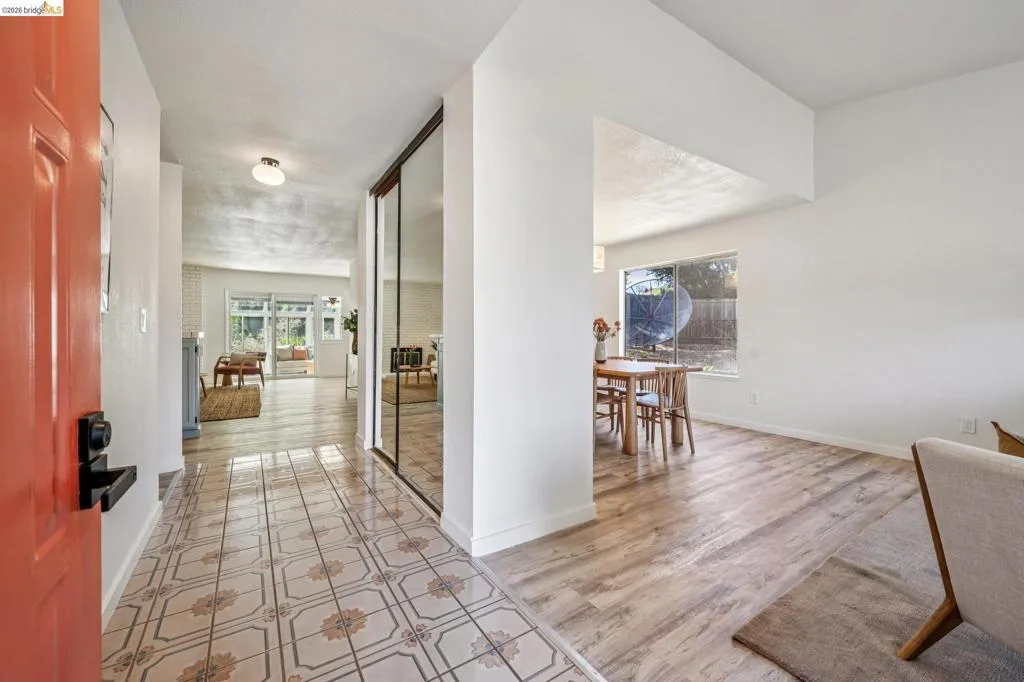 Entryway featuring patterned tile flooring, a vibrant orange entry door, and a mirrored closet