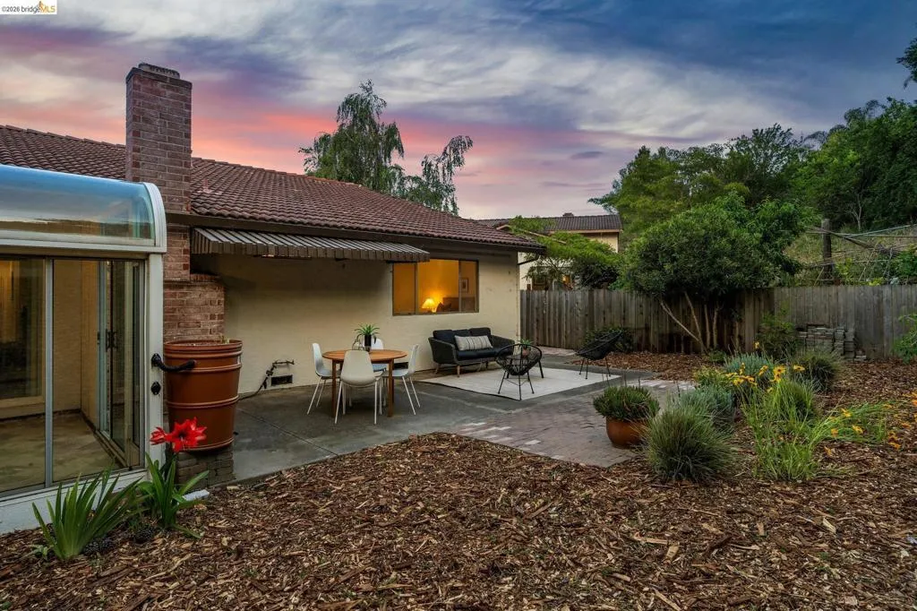 Expansive backyard featuring a brick chimney, a tiled roof, and a covered patio area with a retractable awning