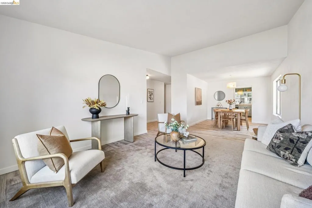 Spacious living area featuring light-colored walls, vaulted ceilings, and plush carpeting