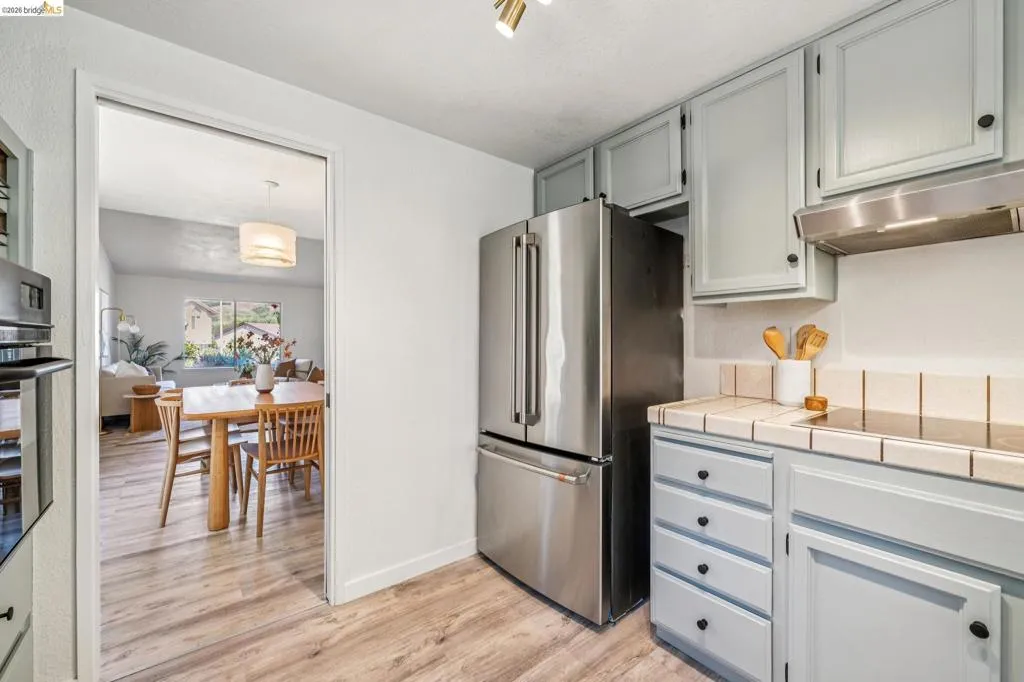 Kitchen featuring light blue cabinetry, tiled countertops, stainless steel refrigerator, and wood-finish flooring