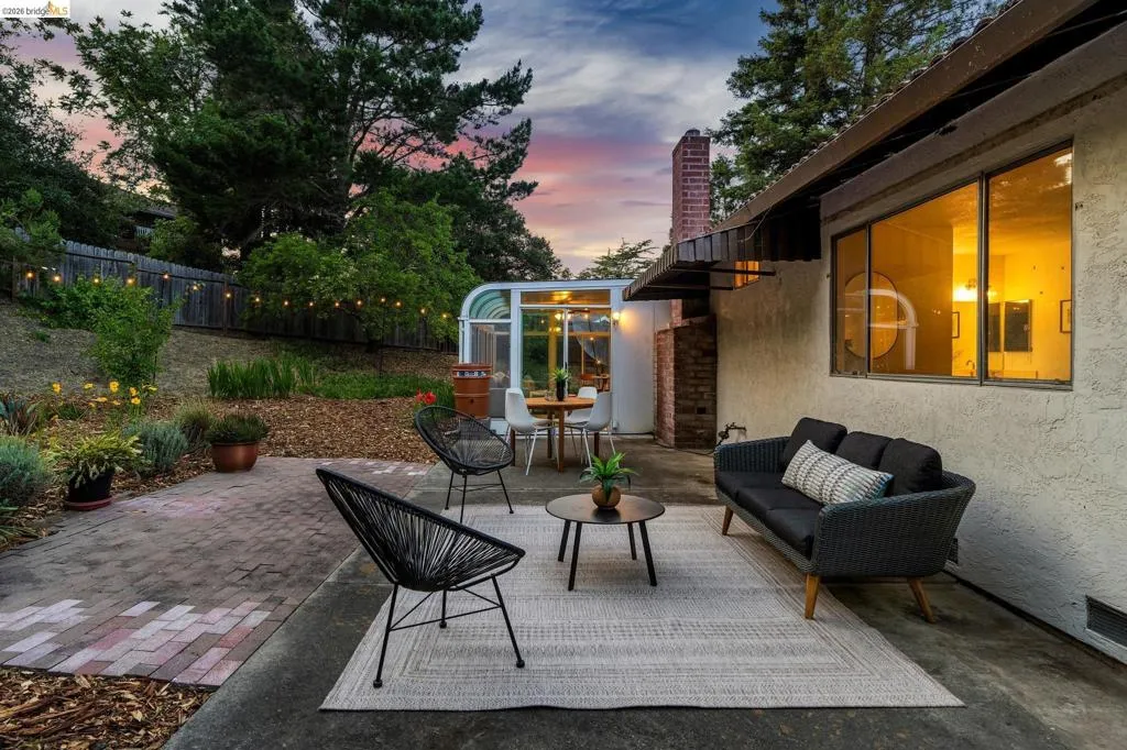 Expansive outdoor patio featuring concrete and brick paving, a greenhouse structure, and a terraced garden area