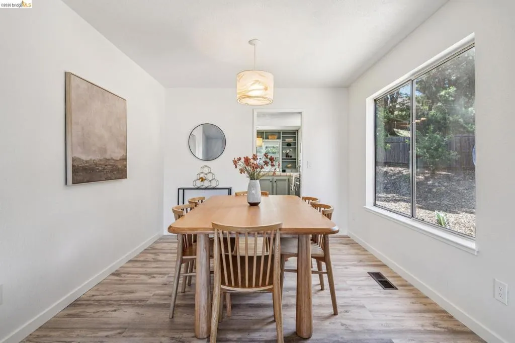 Dining area featuring wood-finish flooring, a contemporary pendant light fixture, and a large window offering exterior views