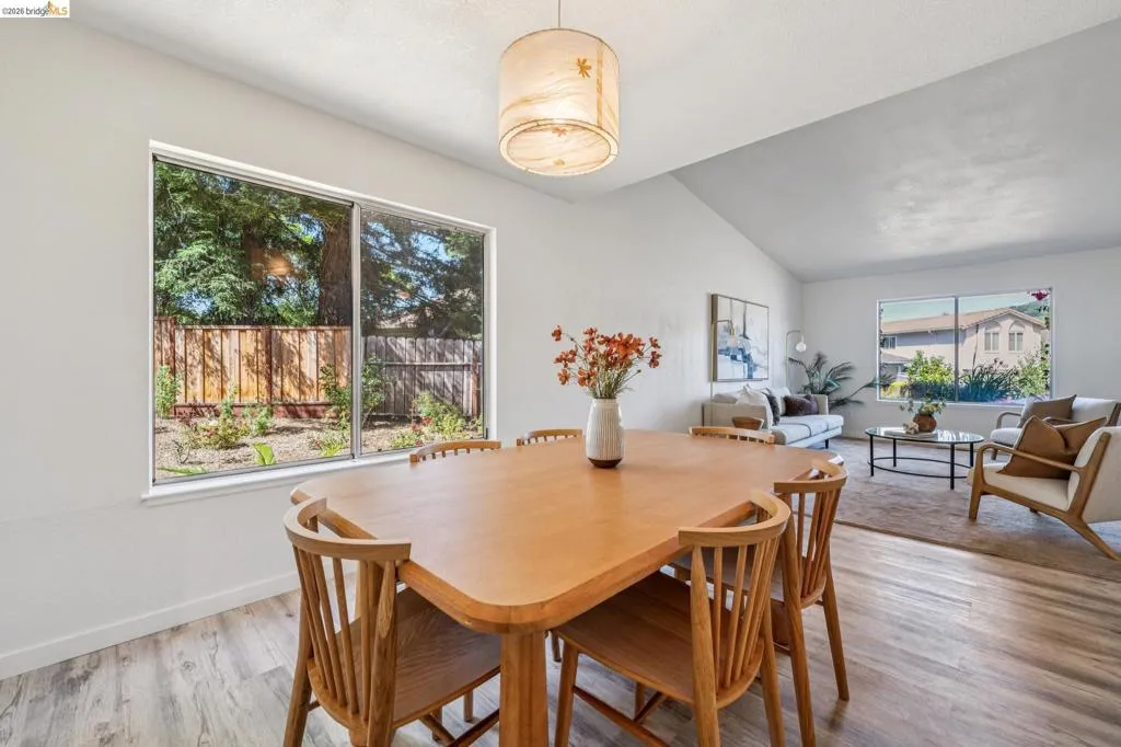 Open-concept dining area featuring wood-finish flooring, a contemporary pendant light fixture, and a large picture window