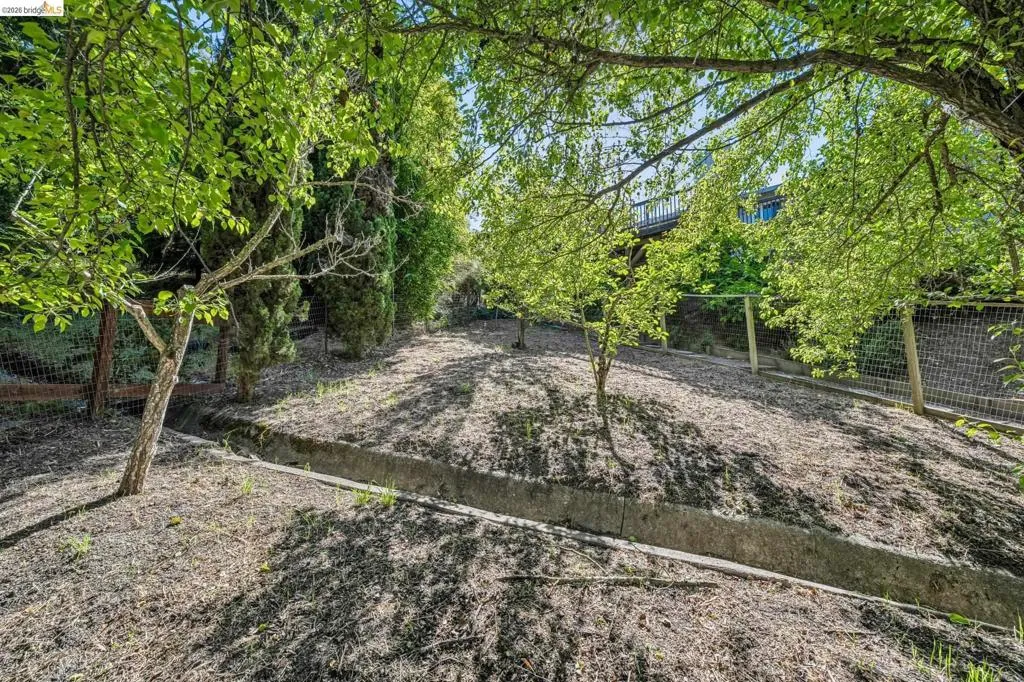 Sloping backyard featuring mature trees, partial chain-link fencing, and a concrete drainage channel