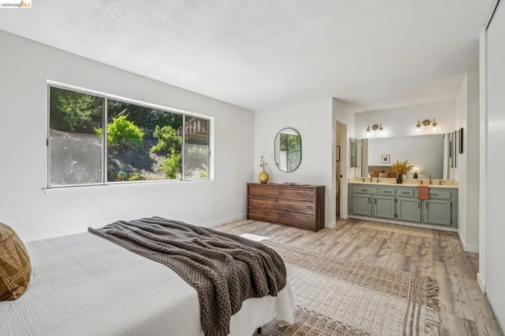 Spacious room featuring wood-finish flooring, a wide window, an integrated double vanity with cabinet storage, and an oval mirror