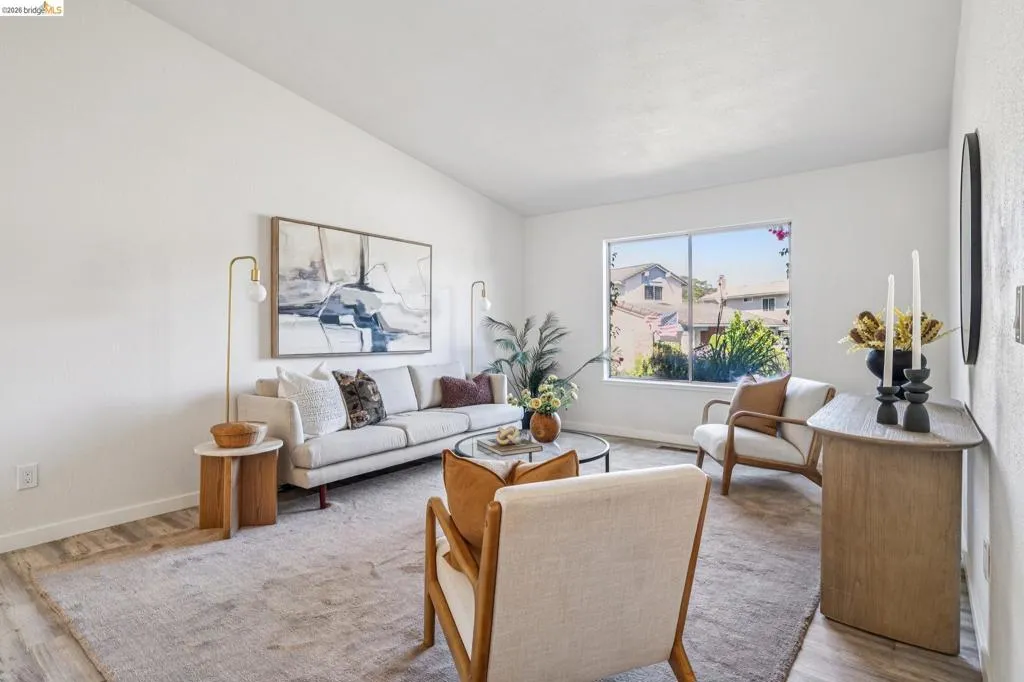 Living area featuring vaulted ceilings, light-hued walls, wood-finish flooring, a large picture window, and a light-toned area rug