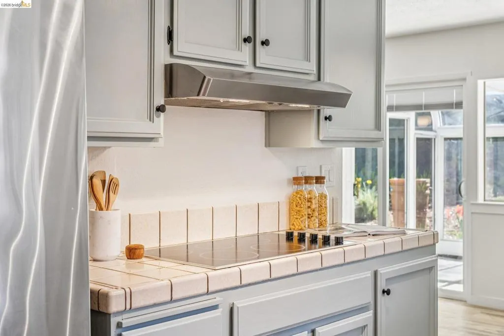 Kitchen featuring light gray cabinetry with black hardware, a stainless steel range hood, and a tile countertop
