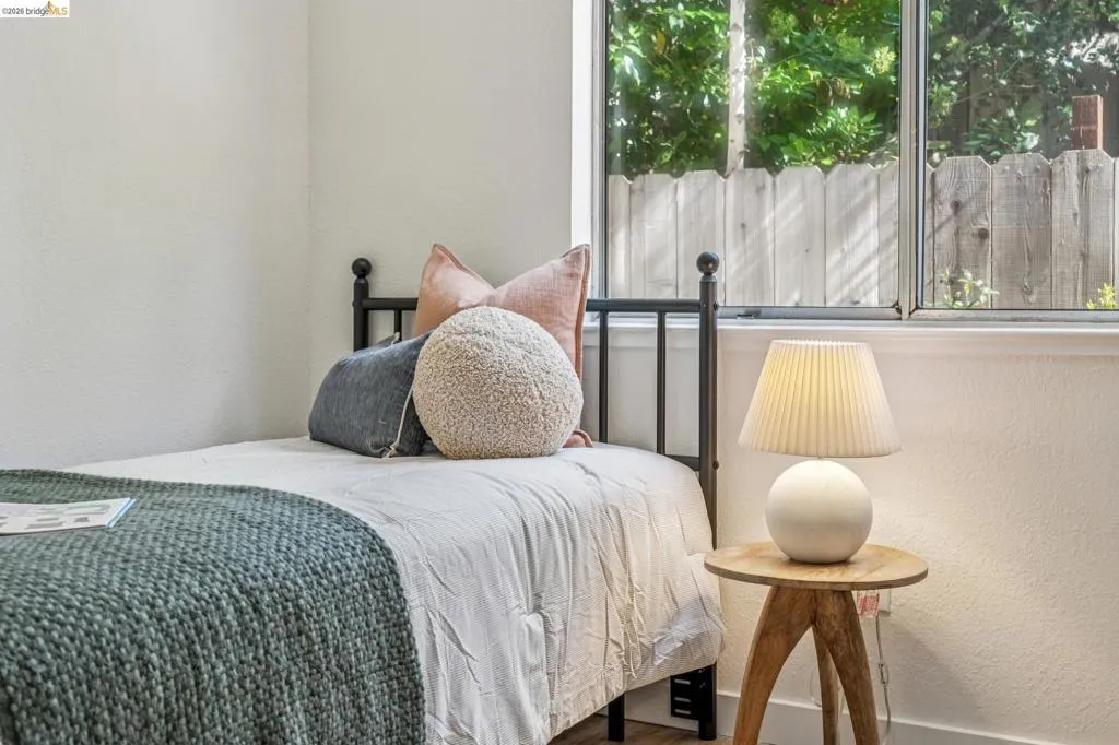 Bright room featuring a window overlooking a wooden fence and greenery, white walls, and wood-finish flooring