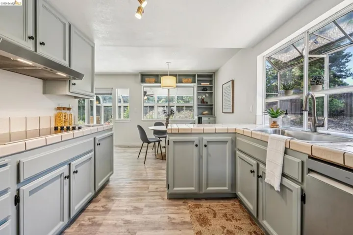 Kitchen featuring light gray cabinetry, tile countertops, a stainless steel sink with a gooseneck faucet, and wood-finish flooring