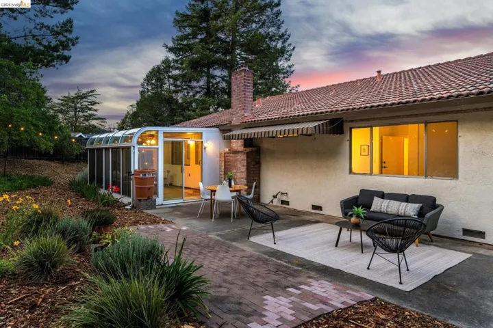 Expansive rear patio featuring a brick paver pathway, a sunroom extension with sliding glass doors, and a red tile roofline