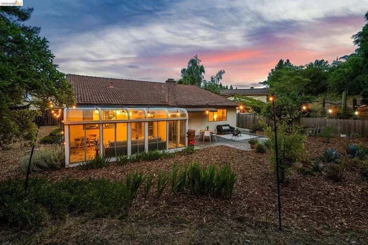 Backyard featuring a sunroom addition with a full glass enclosure, a tiled patio, and a terraced landscape