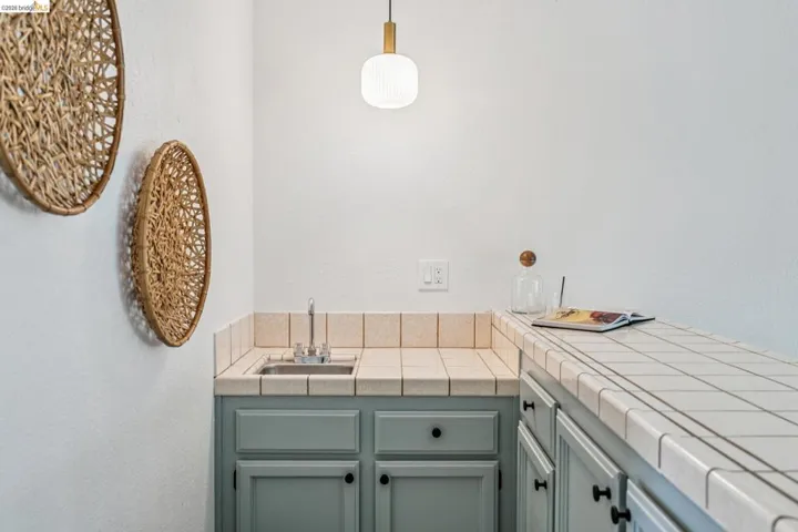 Wet bar featuring a stainless steel sink, tile countertops, light blue cabinetry, and a modern pendant light fixture