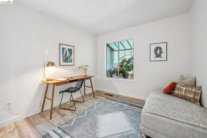Room featuring light wood-finish flooring, white painted walls, and a large window with exterior foliage visible