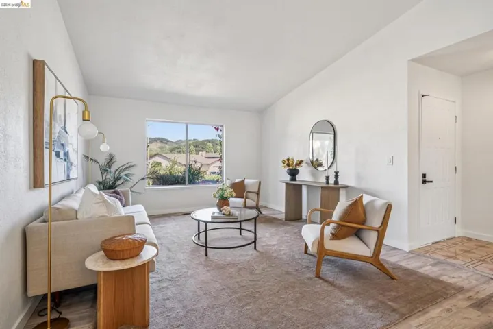 Bright living area with vaulted ceilings, a large picture window, and wood-finish flooring