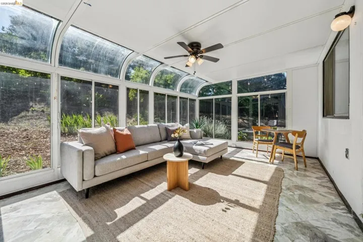 Sunroom featuring a curved glass ceiling, full-height windows, a ceiling fan with integrated lighting, and stone flooring