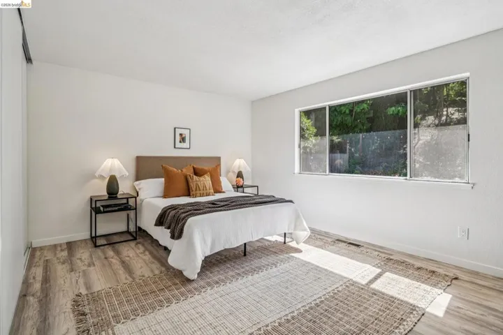 Spacious bedroom featuring wood-finish flooring, a large multi-pane window, and neutral wall tones