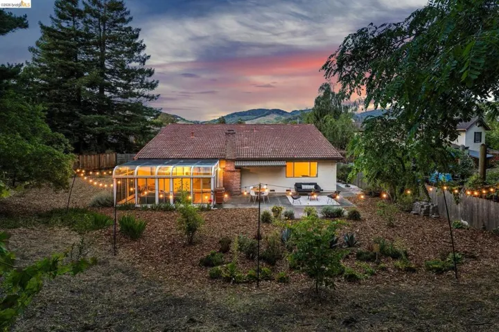 Expansive rear yard featuring an enclosed sunroom, a paved patio, and tiered landscaping