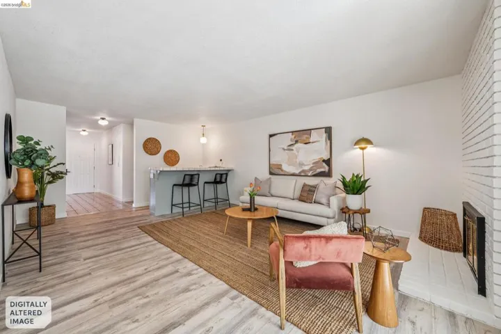 Spacious living area featuring light wood-finish flooring and a white painted brick fireplace