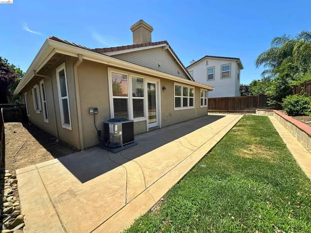 Backyard featuring a concrete patio, a section of lawn, and a retaining wall with stone veneer