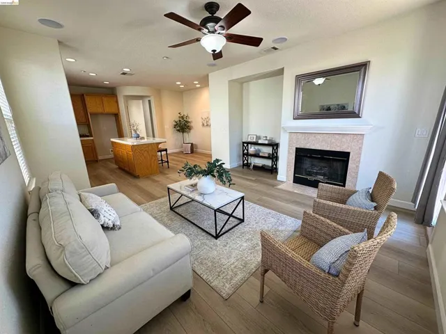 Open-concept living space featuring wood-finish flooring, a ceiling fan with integrated lighting, recessed lighting, and a fireplace with a tiled surround
