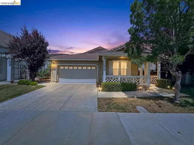 Single-story residence featuring a two-car garage, front porch with decorative railing, and manicured shrubbery