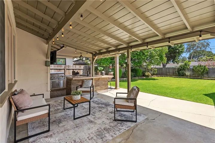 The large covered patio creates a comfortable lounge area with updated pillar lighting, an outdoor fan, and direct views of the spacious backyard lawn.