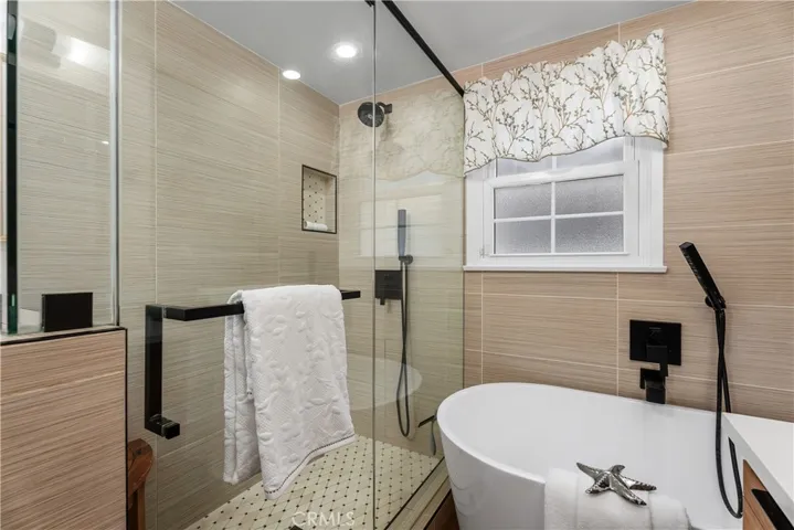 A large walk-in shower with modern tile, frameless glass, inset shelf, and a soaking tub with matte black fixtures continues the bathroom’s elevated, spa-inspired design.