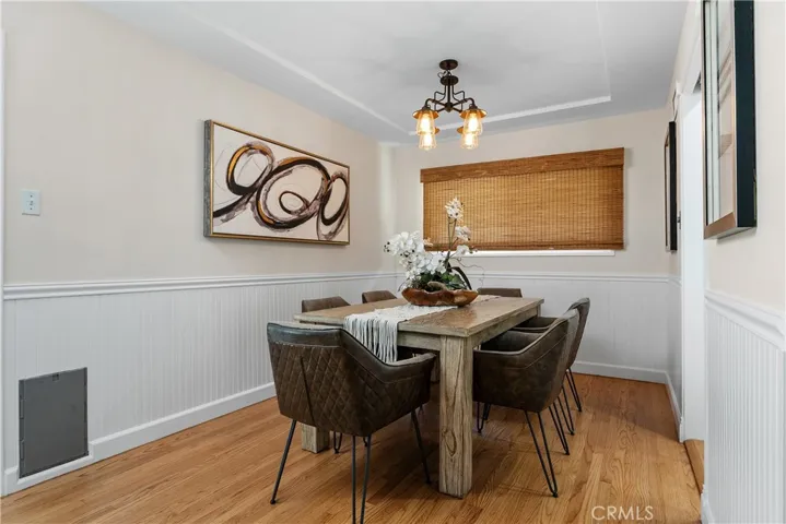 The dining room offers a warm setting for formal dining or everyday gatherings, with wainscoting, updated lighting, bamboo window coverings, and architectural ceiling detail.