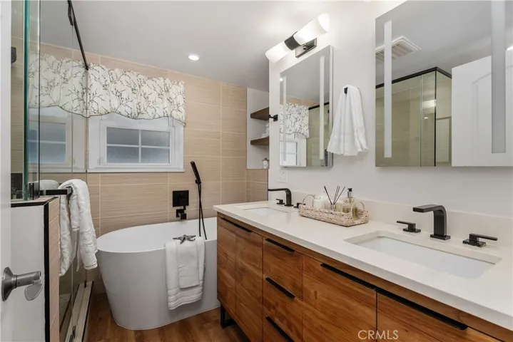 The fully remodeled bathroom feels spa-like with designer finishes, dual vanities, acacia wood cabinetry, matte black fixtures, LED mirrors, and custom built-in shelving.