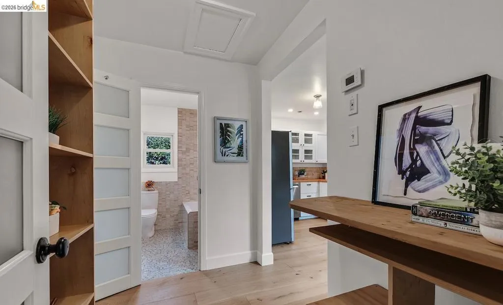 Light wood-finish flooring extending through an open doorway, revealing a kitchen with white cabinetry and a dark refrigerator