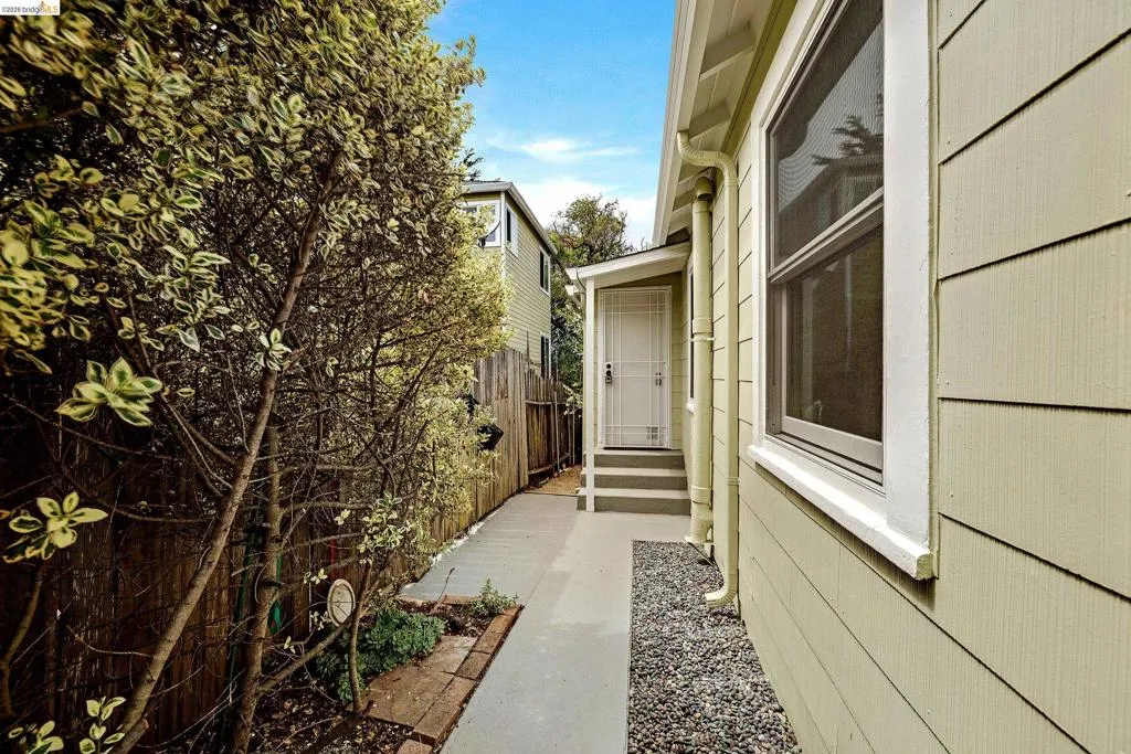 Side exterior featuring horizontal siding, white trim windows, a gravel bed, and a paved walkway leading to a porch with white steps and a security screen door