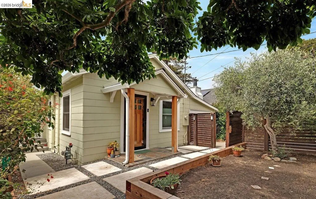 Exterior of a light green clapboard house featuring a covered front entry with a natural wood door and pillar
