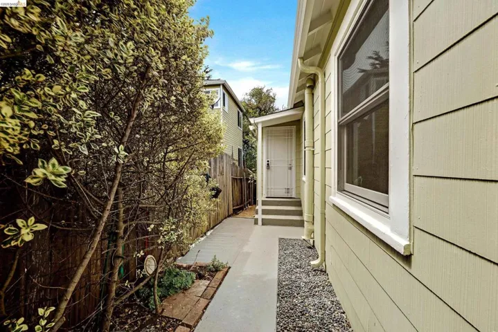 Side exterior featuring horizontal siding, white trim windows, a gravel bed, and a paved walkway leading to a porch with white steps and a security screen door