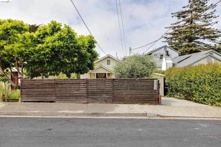 Fenced front yard with horizontal wood paneling, mature tree, and concrete sidewalk