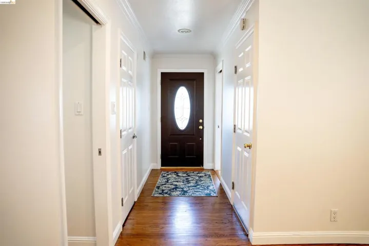 Entryway featuring a dark wood front door with an oval glass insert, wood-finish flooring, white crown molding, and white interior doors with brass hardware